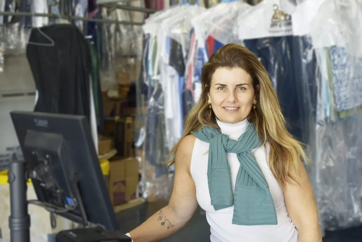 A JM Cleaners team member smiling at the front counter, with freshly cleaned garments on the racks behind her